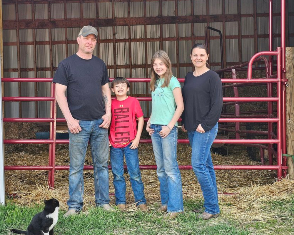 Family of four standing in a barn with a cat nearby